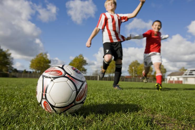 Nahaufnahme eines Fußballs auf einem Rasenfeld, während zwei Kinder im Hintergrund spielen.