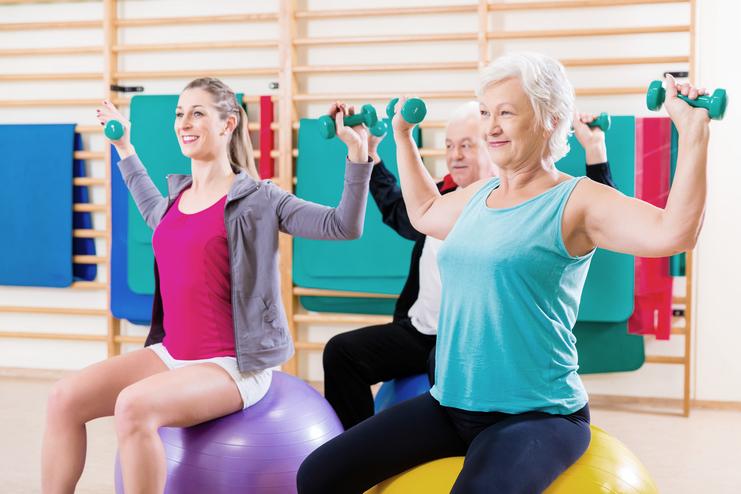 Drei Personen mit Hanteln sitzen auf großen Gymnastikbällen und trainieren in einem Fitnessraum.